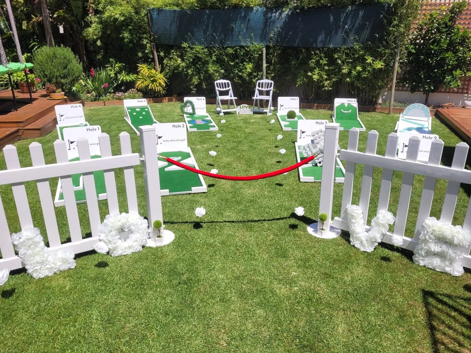 Elegant white picket fence entrance with floral wreaths and red velvet rope at Melbourne wedding mini golf