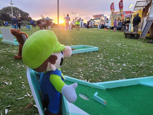 Lucky Shot Mini Golf course set up at a Melbourne outdoor venue at sunset with a Luigi character cutout in view