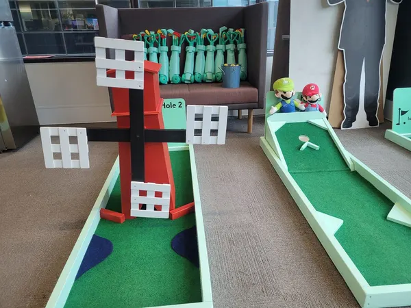 Lucky Shot themed mini golf course at a Melbourne office with red windmill obstacle, Mario and Luigi plushies and putters lined up ready to play